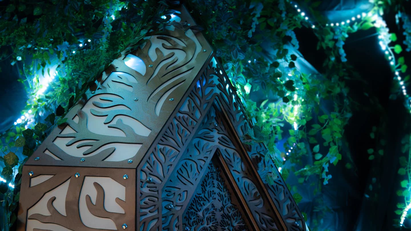A close view of ITU's hanging plywood crystal glowing red and warm white beneath artificial greenery.